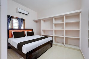 A bedroom with a bed, built-in shelving, an air conditioning unit, and a window with curtains.
