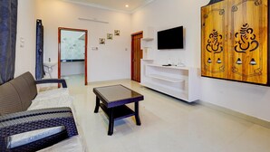 A living room with a sofa, a coffee table, a TV, a wooden wardrobe, and a ceiling fan. - Classic Chhathrapathi Residency (Tirupati)
