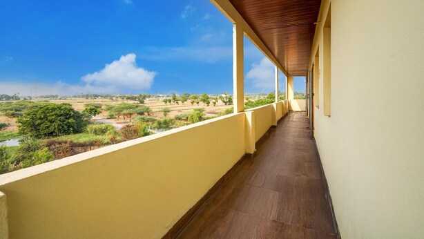 A covered balcony with a view of a rural landscape. - Classic Chhathrapathi Residency (Tirupati)