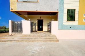 A building with a set of concrete steps leading to a door, a small porch area, and a window with a green curtain.