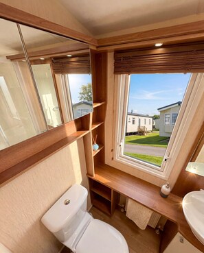 Ein kleines Badezimmer mit Toilette, Waschbecken und einem Fenster mit Blick auf ein Wohngebiet.