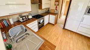 Une cuisine de taille réduite, équipée d’un évier, d’une cuisinière et de meubles blancs.