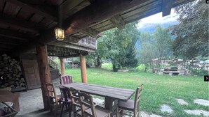 An outdoor patio with a wooden table and chairs, a lantern, and a stone floor.