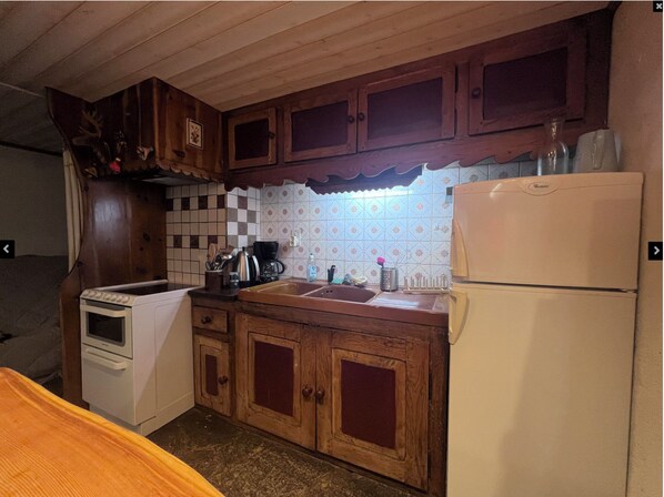 Une cuisine avec des meubles en bois, un réfrigérateur blanc, une machine à café et une cuisinière.