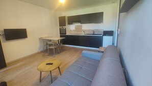 A modern living room with a grey sofa, a small wooden table, and a TV mounted on the wall.