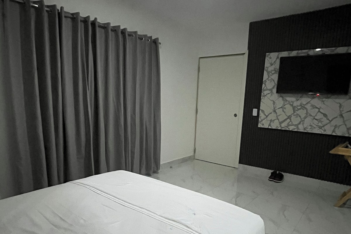 A bedroom with a bed, curtains, a TV mounted on the wall, and a door.