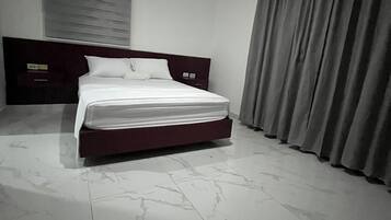 A bedroom with a bed, a headboard, a window with blinds, and a curtain.