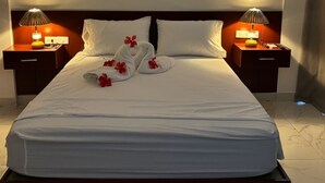 Una habitación de hotel con una cama grande, dos mesitas de noche con lámparas y suelo de mármol.