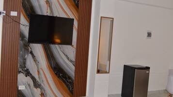 A room with a flat-screen TV mounted on a wall with a marble-like design, a small trash bin, and a mirror on the wall.