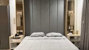 Un dormitorio moderno con una cama grande, mesitas de noche, un armario y un baño visible a través de una puerta abierta.