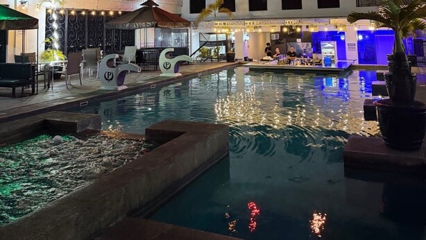 Zona de piscina nocturna con bar y asientos, rodeada de edificios.