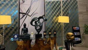 Un vestíbulo moderno con una mesa de centro de vidrio, dos lámparas, una estatua de Buda y una escultura de madera.