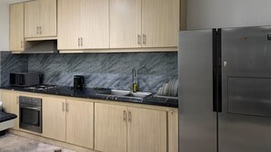 Una cocina con armarios de madera clara, encimera negra, refrigerador de acero inoxidable y microondas.