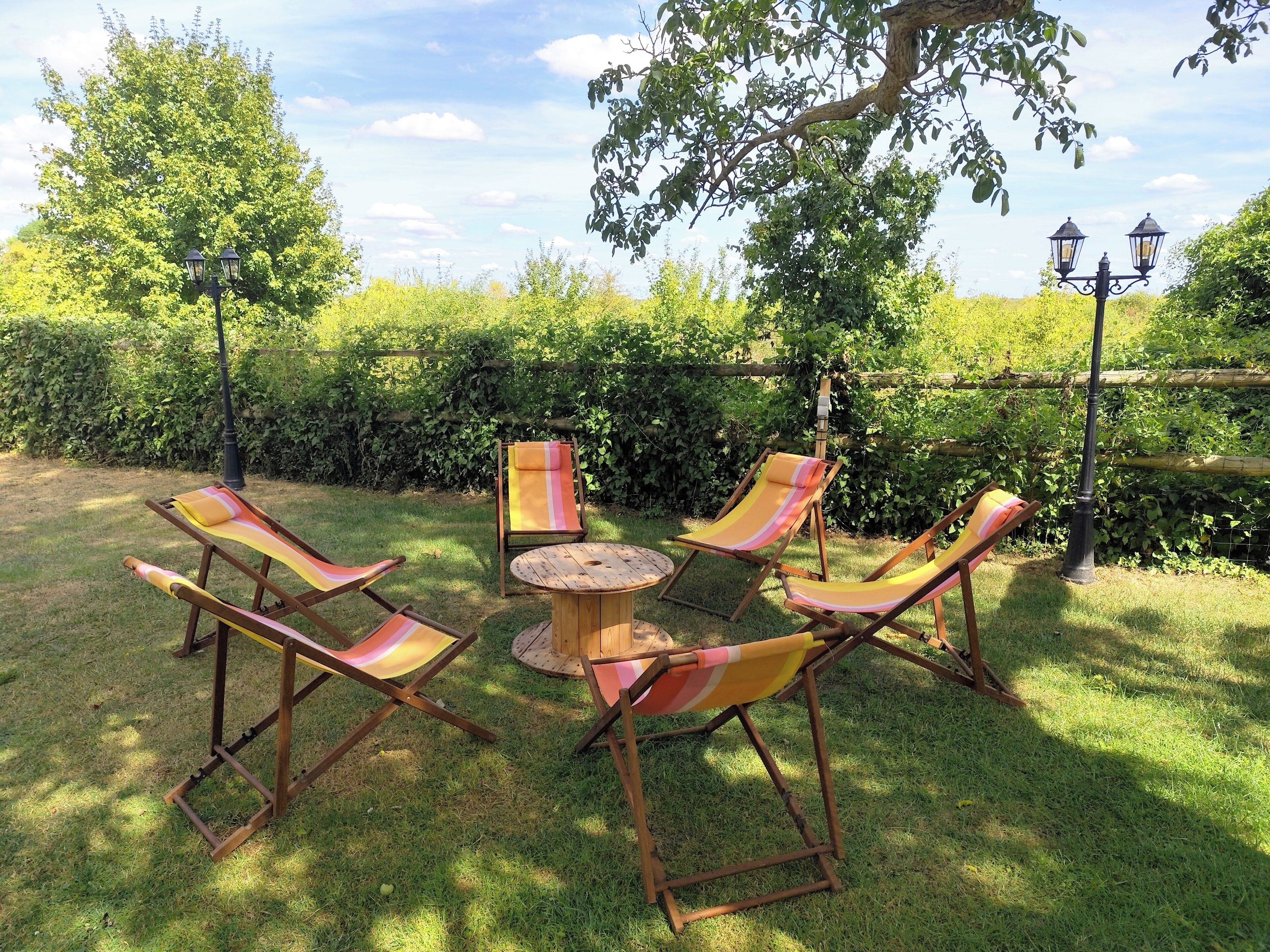 Un jardín con una mesa de madera y cuatro sillones a rayas.
