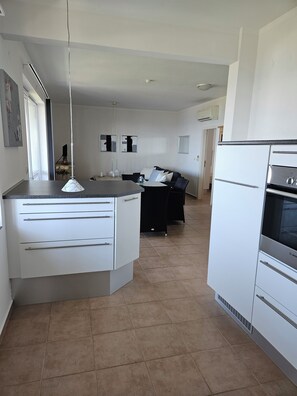 A modern kitchen with a central island, white cabinetry, and a built-in oven. - Vacation apartment Byala Black Sea (Byala)