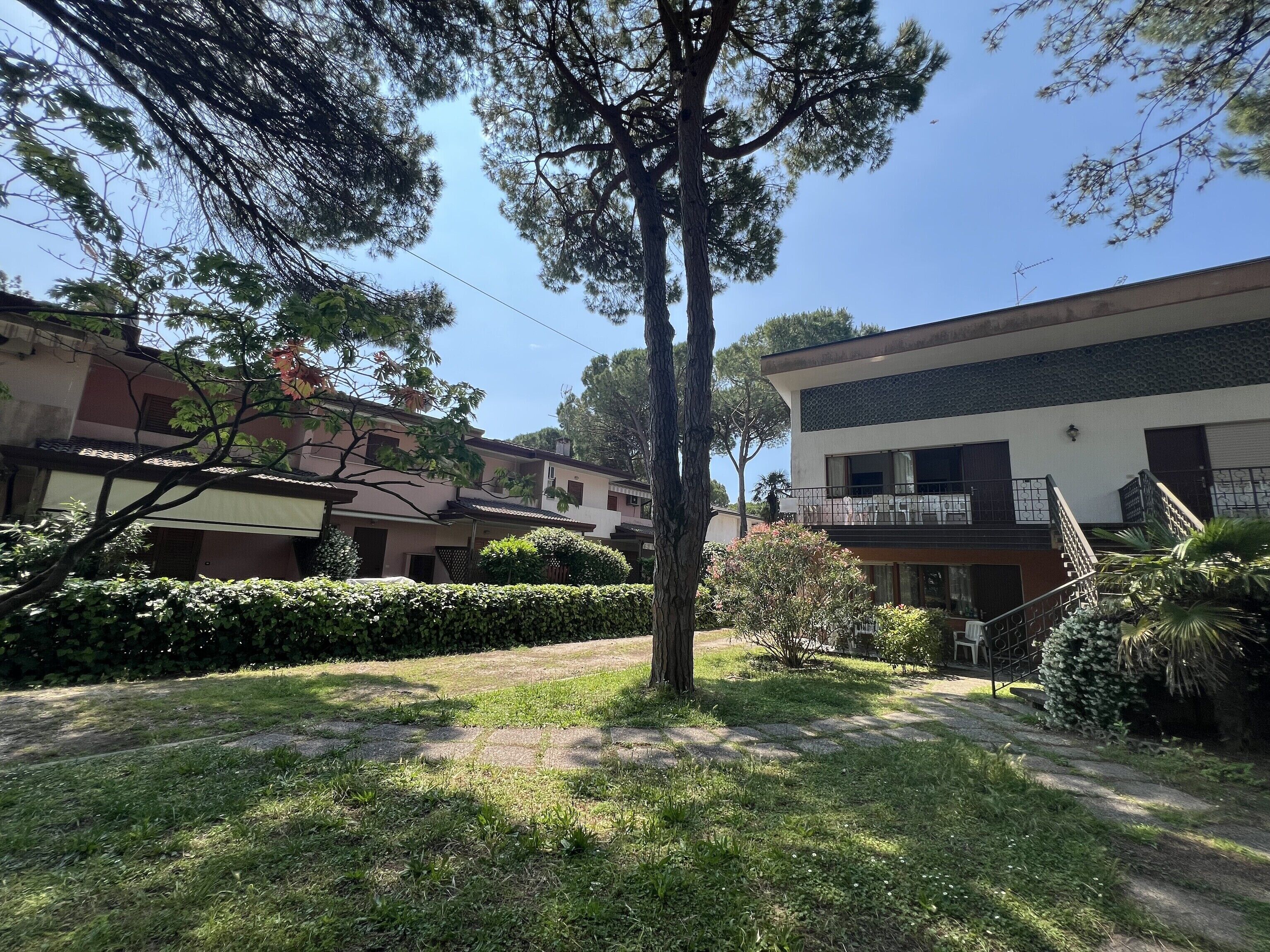 A residential area with a tree-lined pathway, a modern building with a balcony, and a staircase leading to an upper floor.