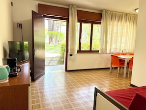 Ein Zimmer mit einem Bett, einem Fernseher, einer Kaffeemaschine, einem Tisch mit Stühlen und einem fensterbepflanzten Fenster.