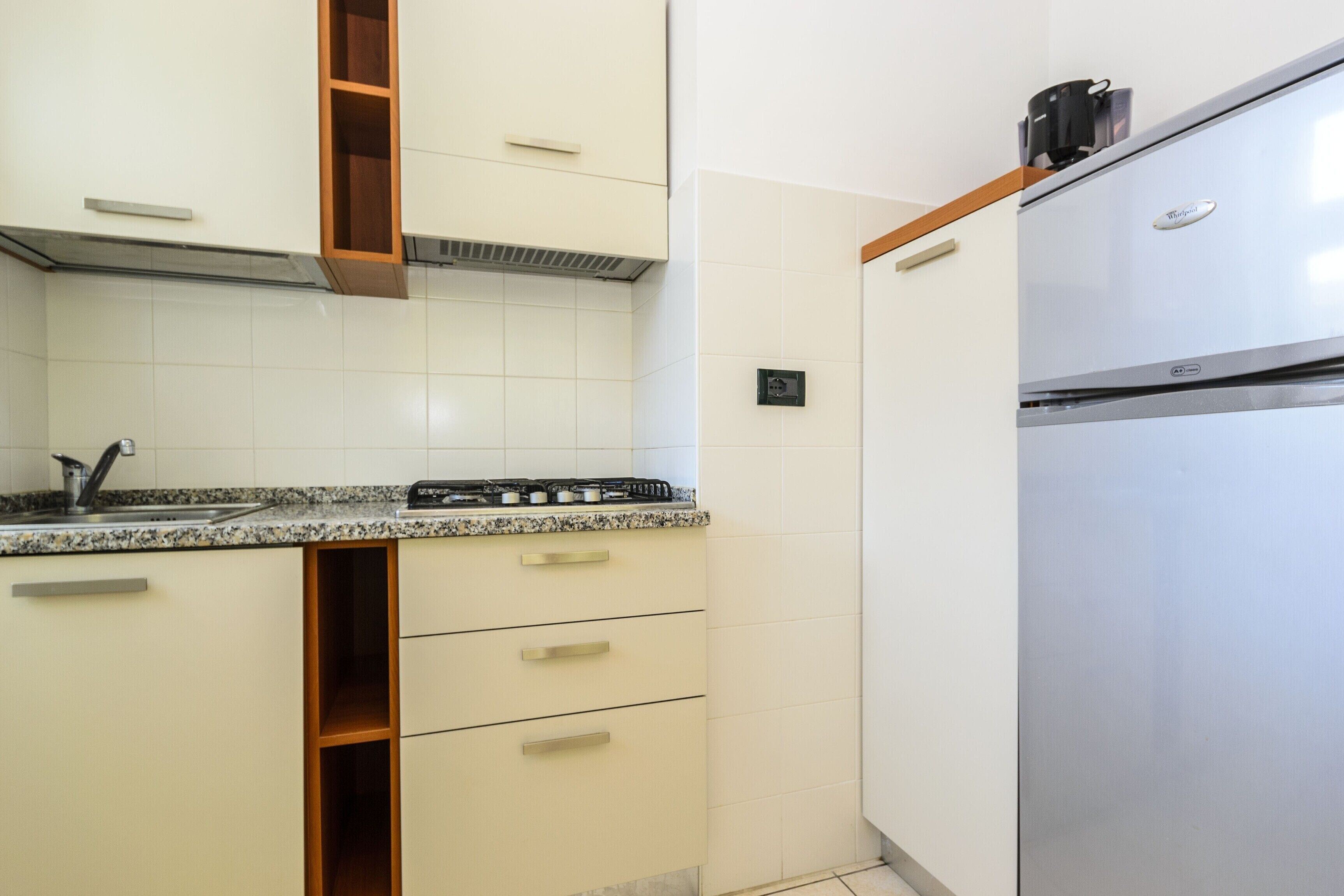 Una cucina con mobili bianchi, un frigorifero in acciaio inossidabile e un piano di lavoro in granito.