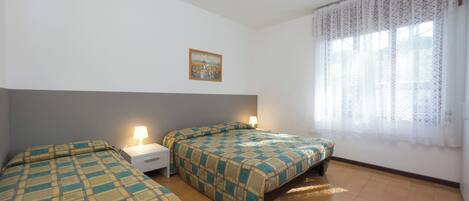 Una habitación con dos camas, una mesita de noche, una lámpara, un cuadro y una ventana con cortinas.