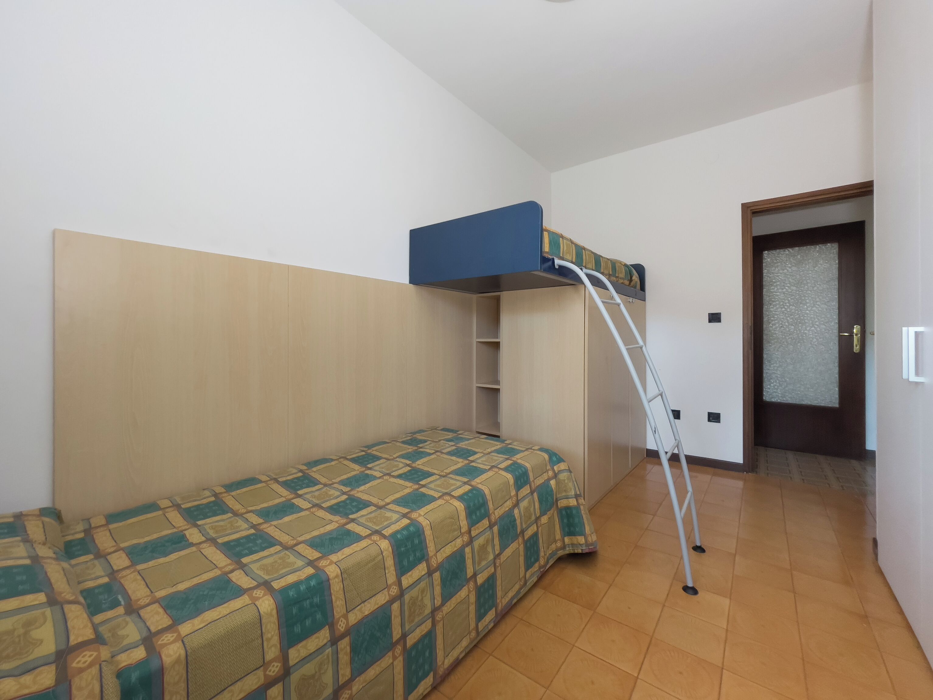 A small room with a bunk bed, a ladder, a wardrobe, and a door.