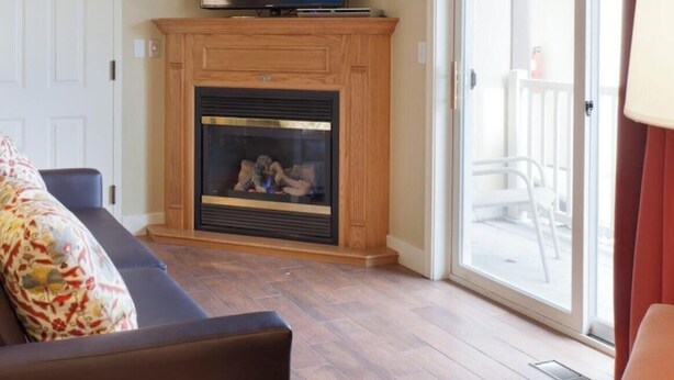 Ein Wohnzimmer mit Kamin, Fernseher auf einer Konsole, einer Couch und Blick ins Freie.