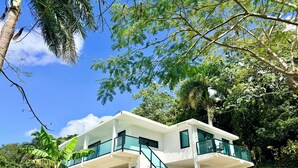 Une maison moderne à deux étages, dotée d’un patio couvert, de grandes fenêtres et offrant une vue sur la verdure environnante.