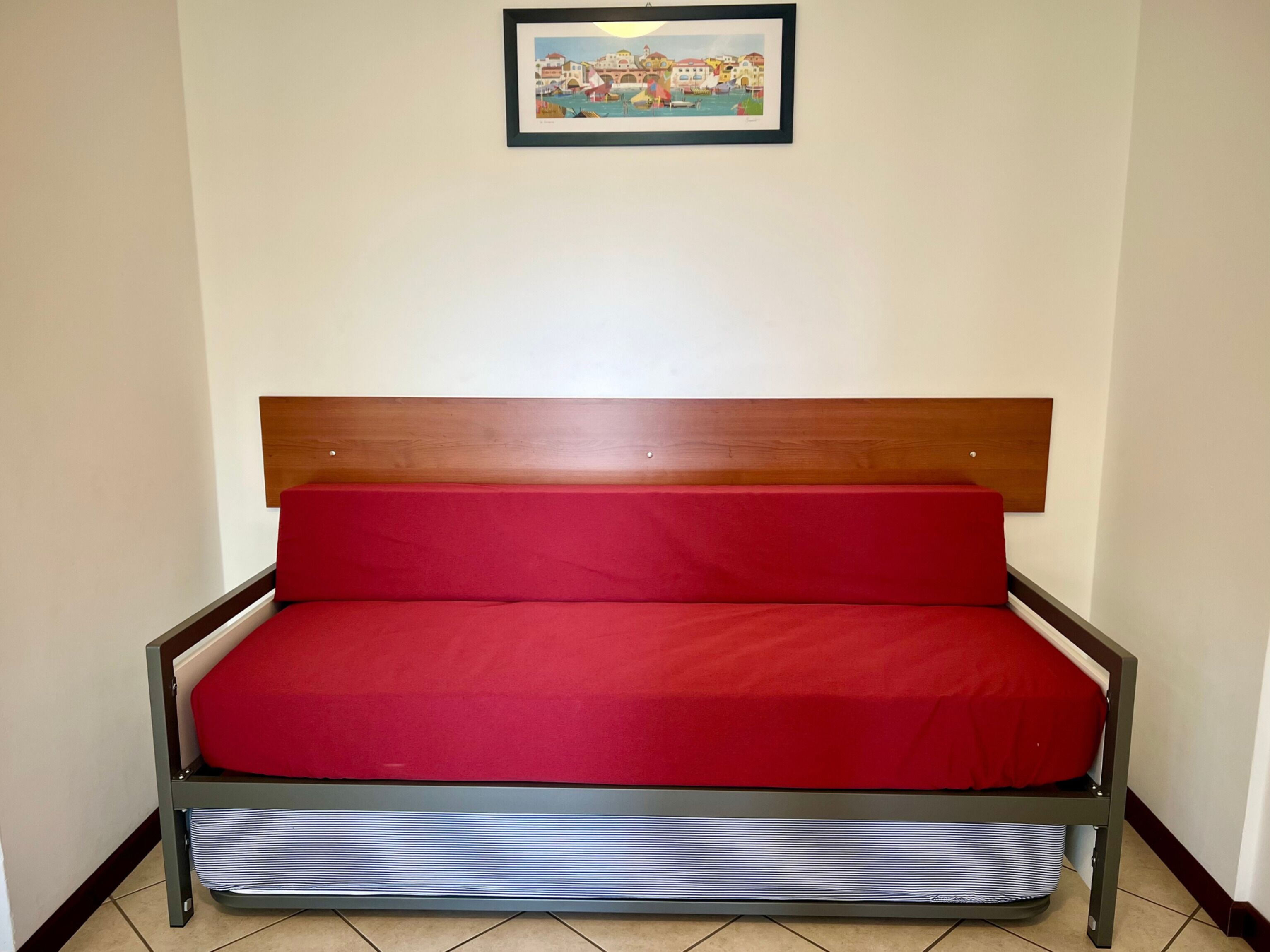 Ein Einzelbett mit Holz Kopfteil, roter Bettwäsche und einem gestreiften Kopfkissen.