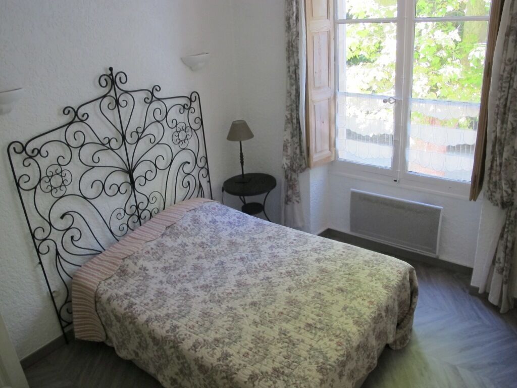 Une chambre à coucher avec un lit, un radiateur, une fenêtre avec des rideaux et une petite table avec une lampe.