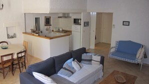 A living room with a sofa, a coffee table, and a dining area with a table and chairs. - Charming apartment at the foot of the Luberon ochres (Rustrel)