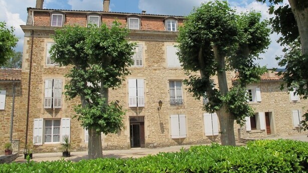A stone building with multiple windows and shutters, surrounded by greenery. - Charming apartment at the foot of the Luberon ochres (Rustrel)