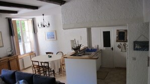 A living room with a sofa, a dining table, and a kitchen area with a sink and cabinets. - Charming apartment at the foot of the Luberon ochres (Rustrel)