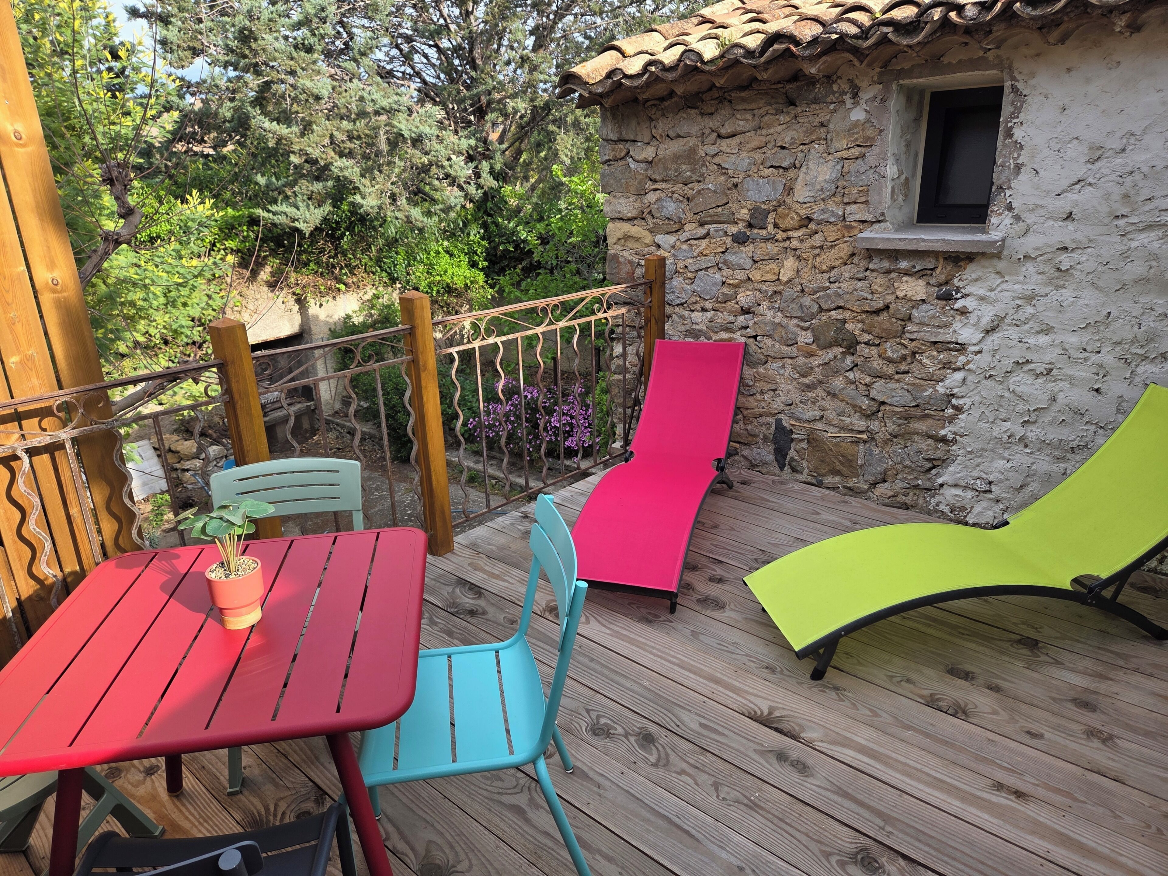 A wooden deck with a stone wall, a small window, and outdoor furniture including a table and chairs.