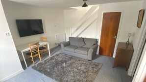 Una sala de estar con un sofá, un sillón de cuero marrón, un televisor, una escalera y una puerta.