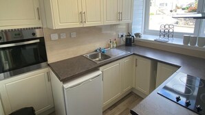 Cocina compacta con armarios blancos, horno integrado, lavavajillas y ventana con vista a la calle.
