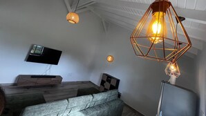Un salon moderne doté d’un téléviseur à écran plat, d’une table basse en bois, d’un canapé gris et d’un luminaire suspendu au design géométrique original.