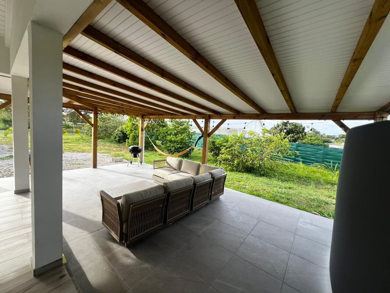 Un espacio al aire libre cubierto con sofá y sillones, una hamaca y vistas a la vegetación.