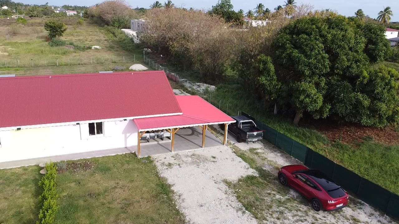 Un bâtiment avec un toit rouge, un espace de stationnement couvert et une voiture rouge garée à l’extérieur.