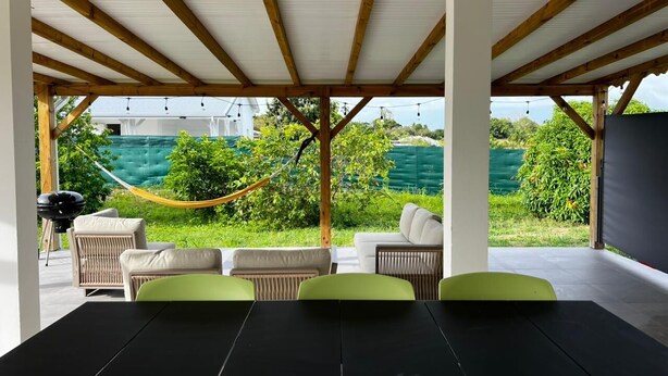 Une terrasse extérieure avec une table et des chaises, un hamac et une vue sur la verdure.