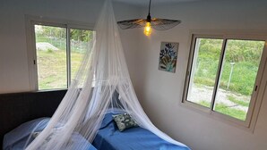 Une chambre à coucher avec un lit placé sous un dais blanc, deux fenêtres et une seule ampoule.