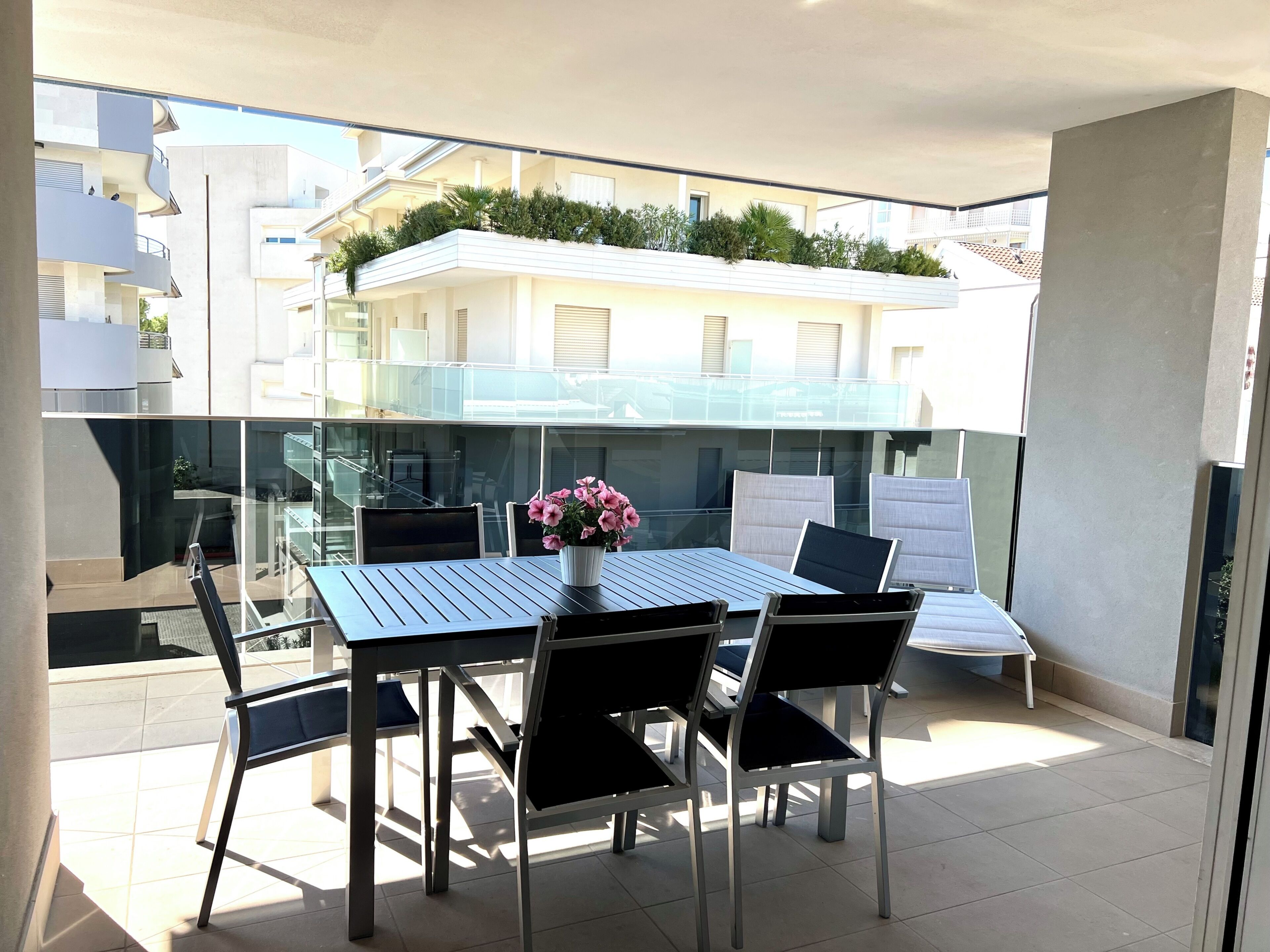 Een balkon met een tafel, stoelen, een bloempot en uitzicht op gebouwen.