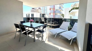 Ein Balkon mit Tisch, Stühlen und einer Liege, mit Blick auf Gebäude.