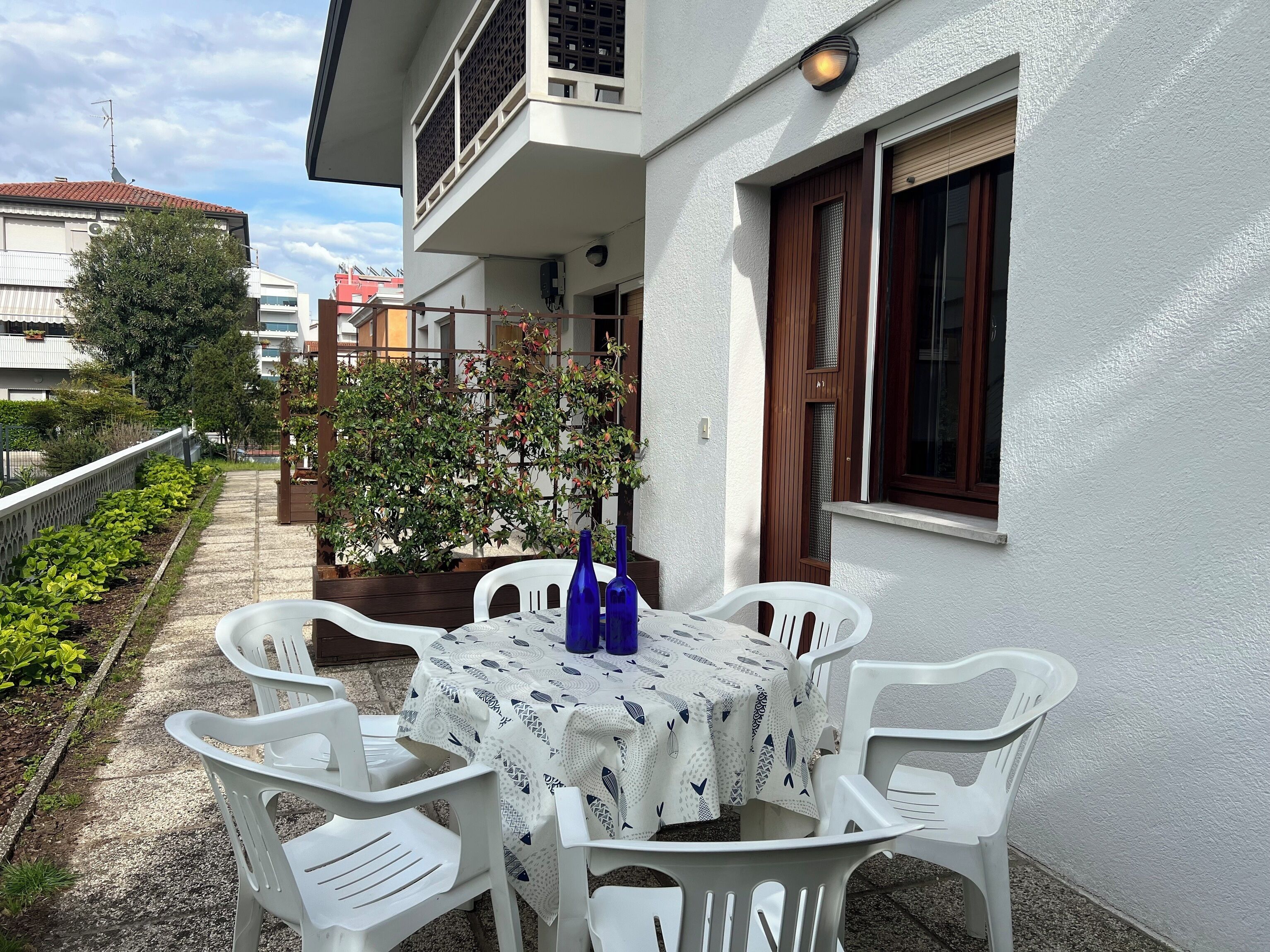 Een terras met een tafel en stoelen, een bloempot en een gebouw met een raam en balkon.