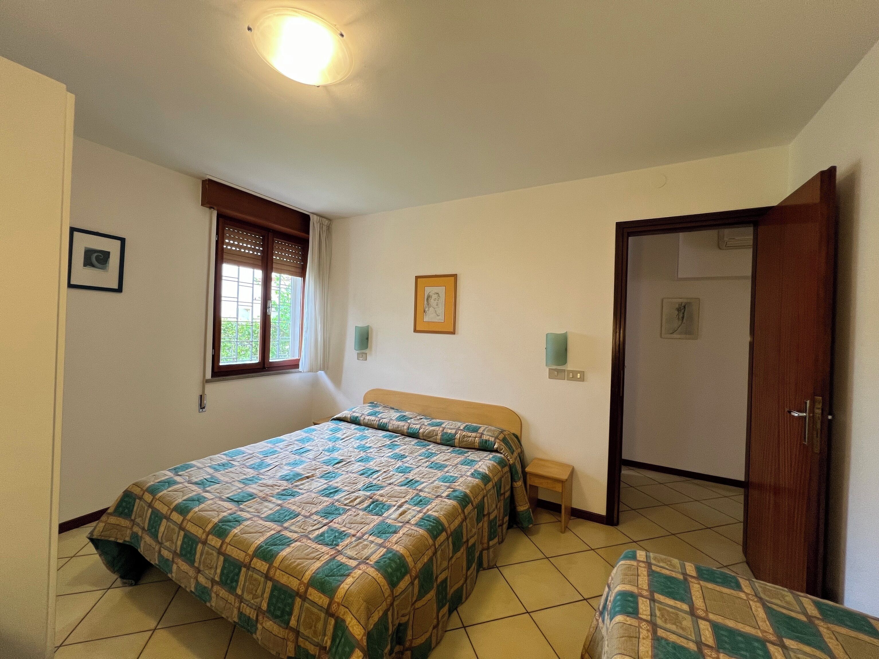 Una habitación con dos camas, una ventana con persianas, una puerta y una lámpara.