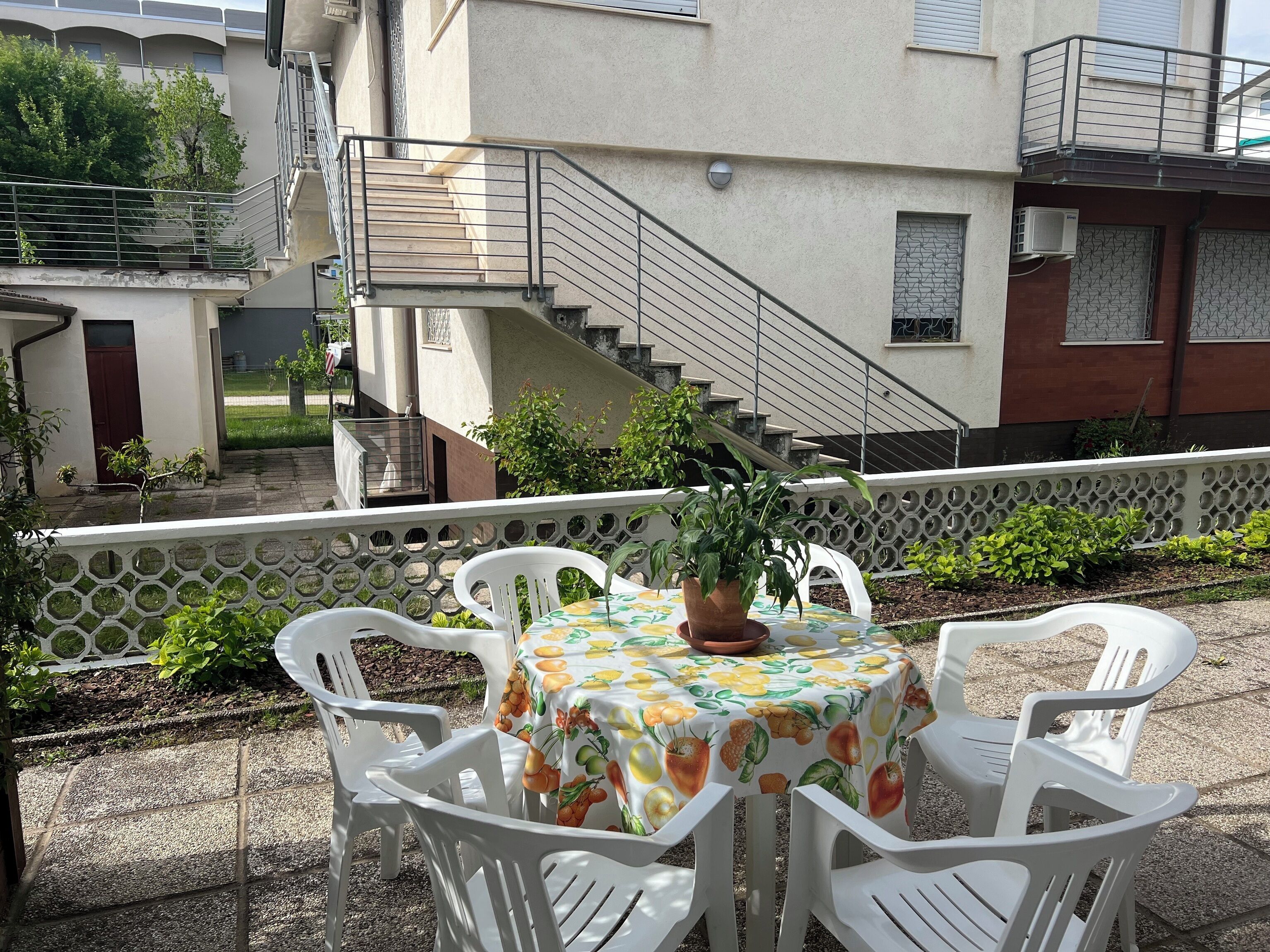 Een terras buiten met een tafel en stoelen, een potplant en een trap naar een hoger gelegen niveau.