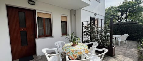 Un patio con una mesa, sillas, una planta en maceta y una puerta con ventanal.