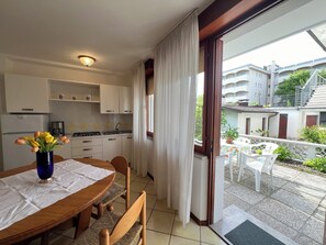 A kitchen with white cabinets, a dining table with a vase of flowers, and a view of a balcony with outdoor furniture. - Lignano Apartment With Terrace (Lignano Sabbiadoro)