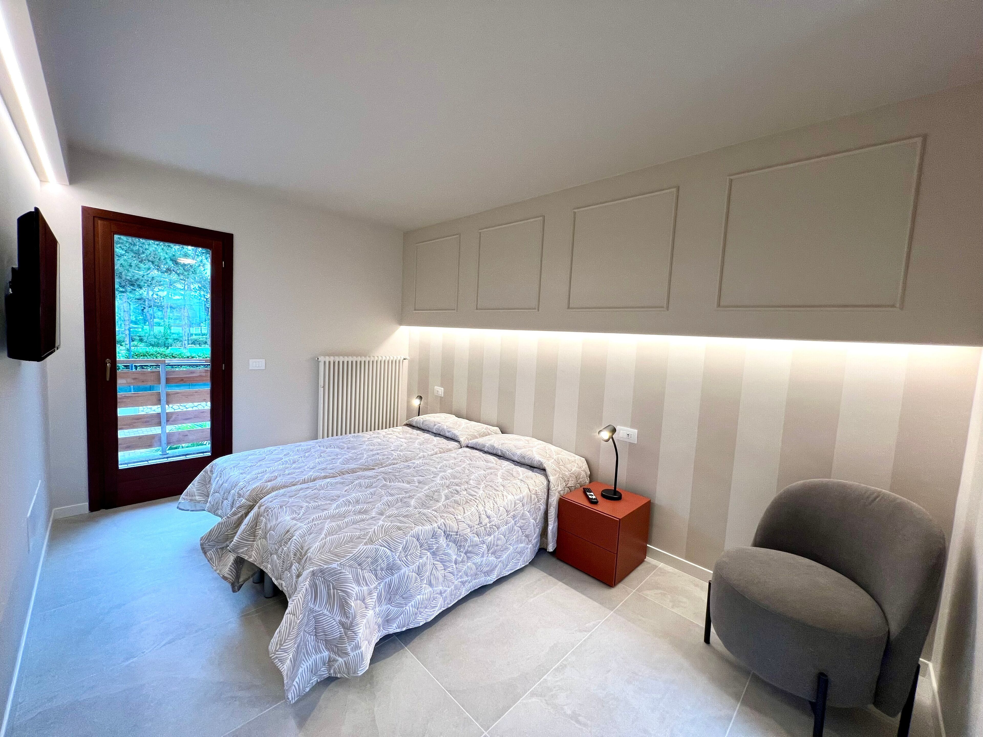 Een slaapkamer met een bed, nachtkastje, stoel, radiator en een deur die leidt naar een balkon.