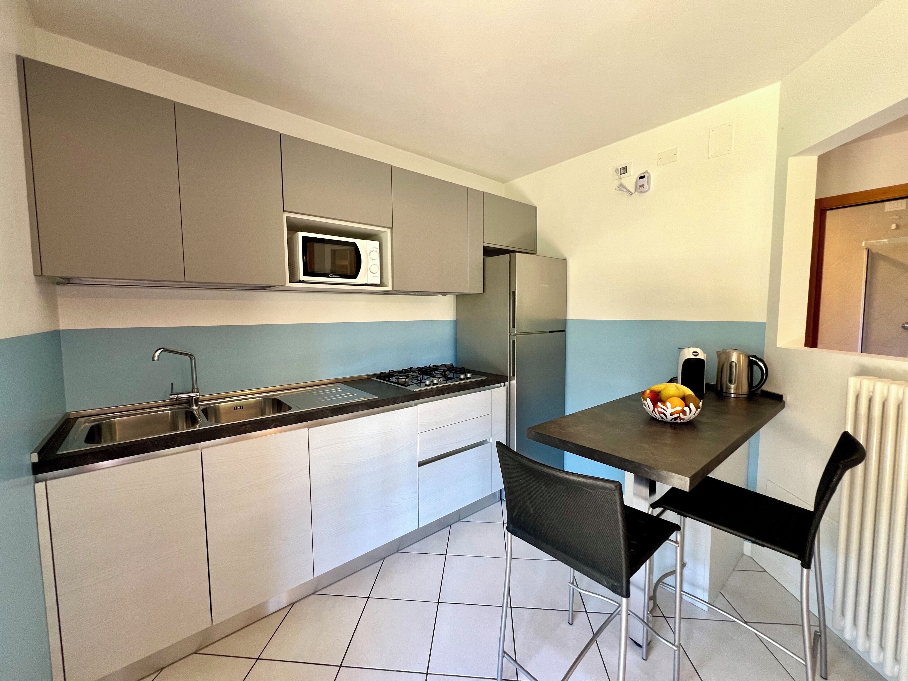 A compact kitchen with a microwave, refrigerator, gas stove, and a small dining table with chairs.
