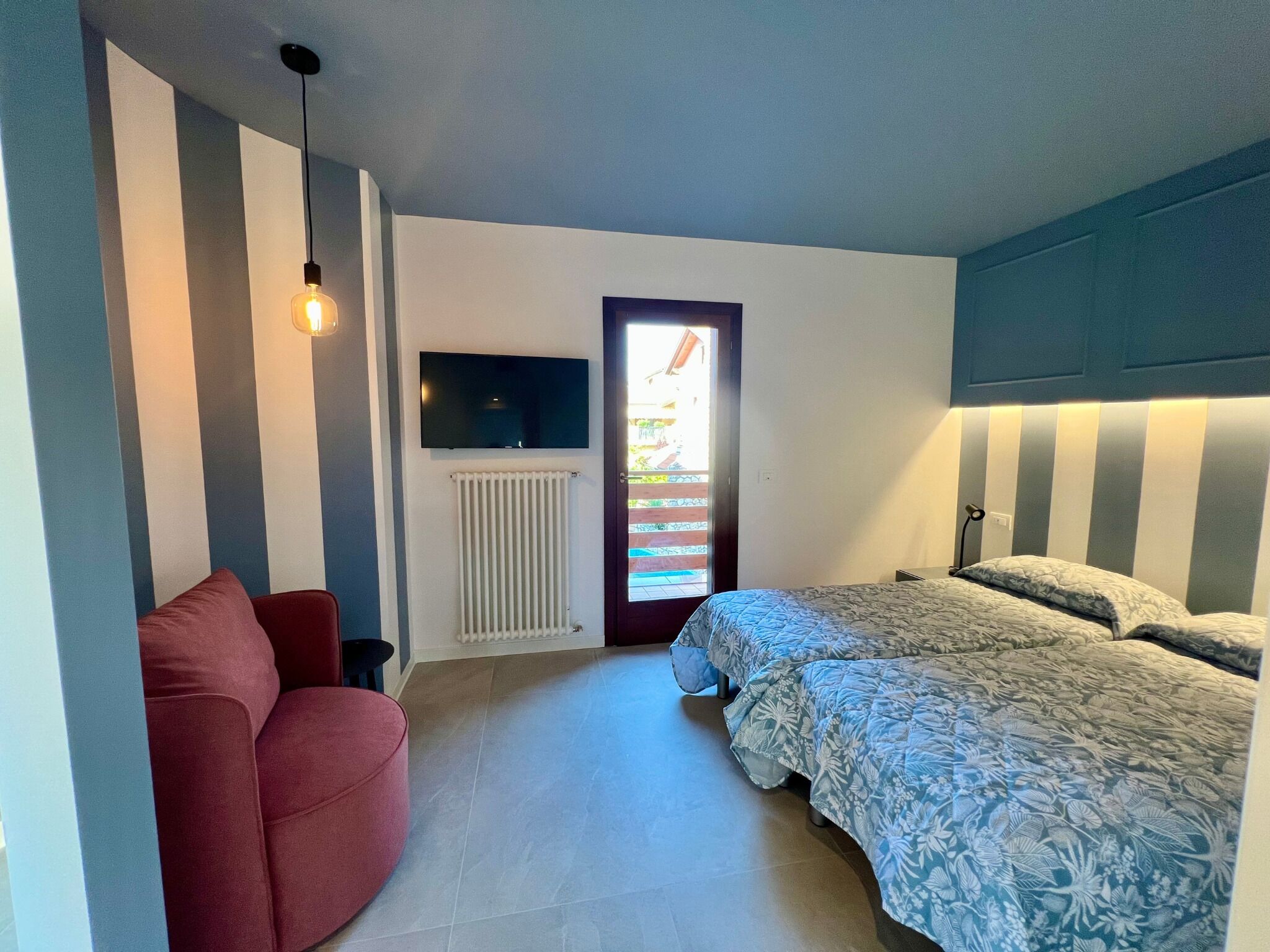 A bedroom with a bed, a red chair, a TV, and a door leading to a balcony.