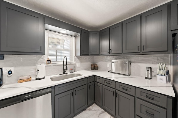 A modern kitchen with grey cabinets, a white countertop, a stainless steel microwave, and a dishwashing unit.